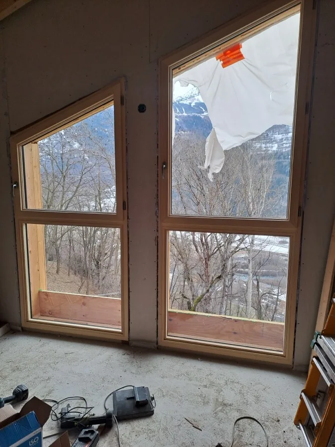 Vue intérieure sur des fenêtres bois donnant sur les montagnes du Jura
