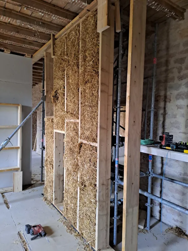 Cloison à ossature bois remplie de bottes de paille, chantier d’éco-construction dans le Jura